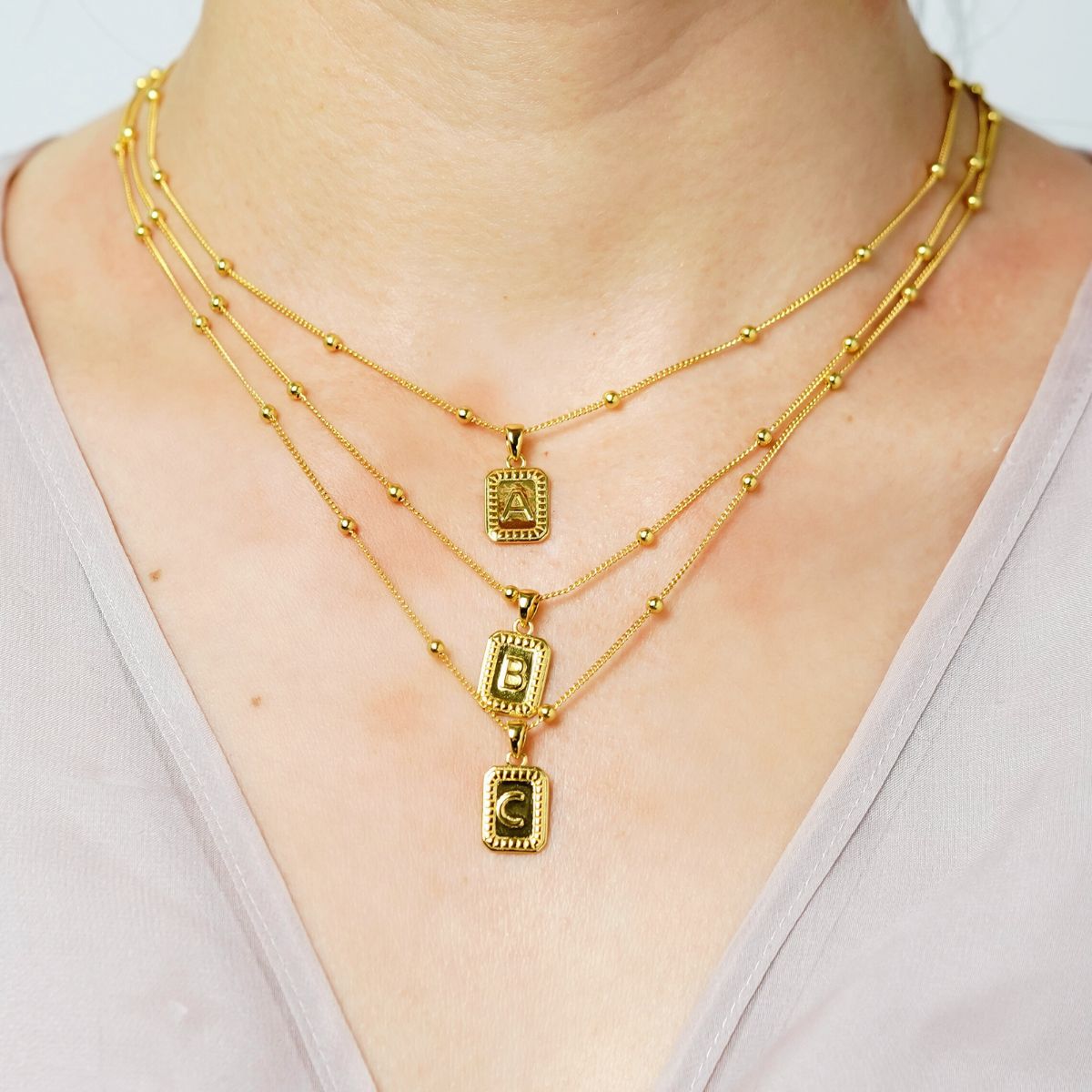 gold initial necklaces with letter A, B, and C necklaces for women layered on model with adjustable chain