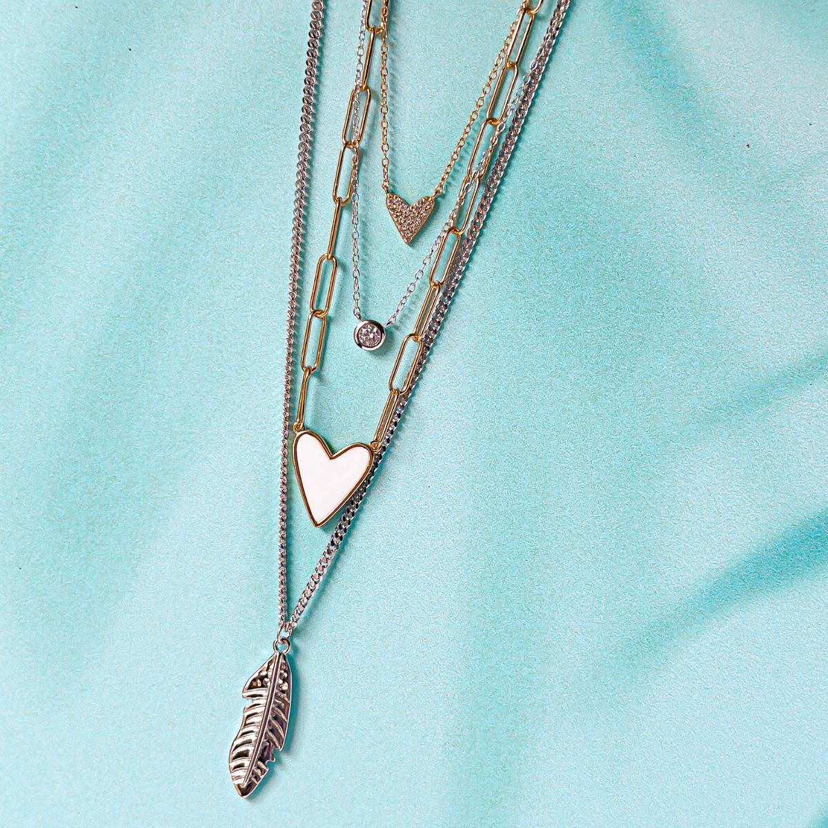 Silver sterling silver and gold layering necklaces from Featherly featuring a feather, hearts, and CZ necklace  stack