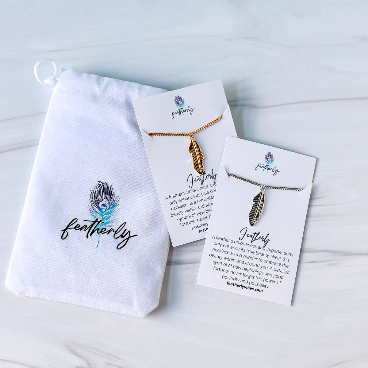 Both silver and gold  feather necklaces on the meaning card with the Featherly white velvet pouch