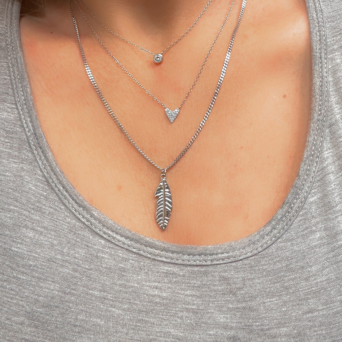 Featherly necklace stack with feather necklace, CZ heart necklace, and solitaire bezel cz necklace all in sterling silver